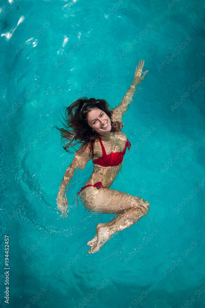 Girl portrait posing underwater with red bikini in swimming pool. beautiful attractive young sexy woman in the swimming pool is swimming on the back