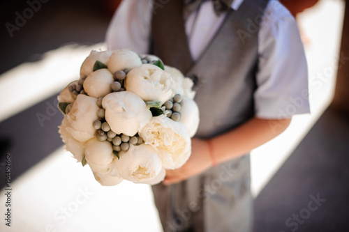 boy holds wedding bouquet from white pion-shaped roses and brunia