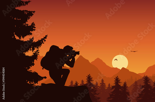 Mountain landscape with forest and tourist photographing flying birds on an orange sky