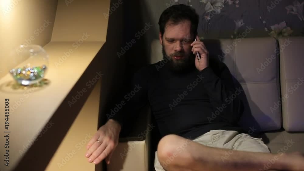 man talking on the phone at home on the couch in the evening man talking on the phone at home on the couch in the evening