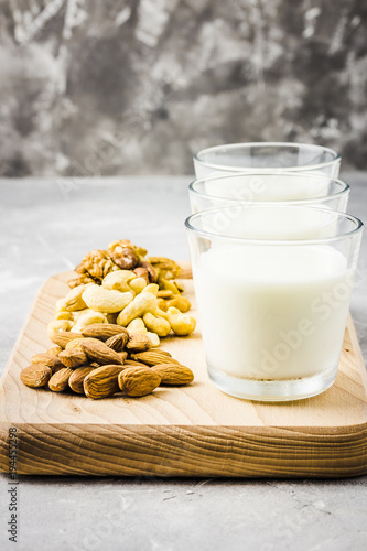 Almonds, cashew, walnuts and nut milk in glasses on wooden board on concrete background. Selective focus, copy space. 