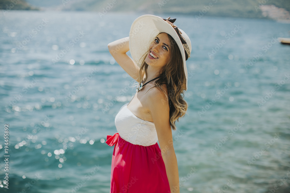 Young attractive woman with a hat poses by the sea at sunny day Young attractive woman with a hat poses by the sea at sunny day