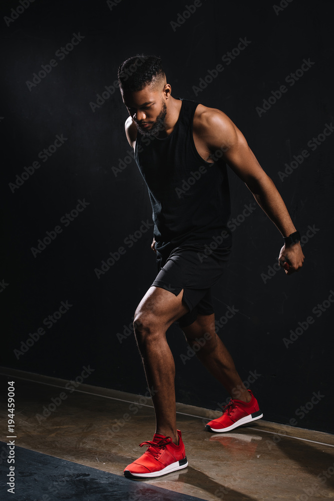 full length view of muscular young african american man in sportswear exercising on black