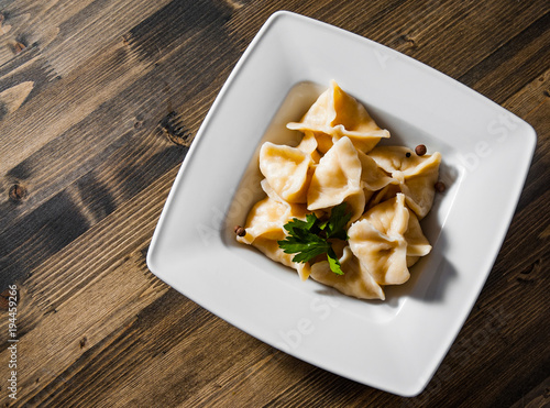 Meat dumplings - russian pelmeni, ravioli with meat on plate on a wooden background