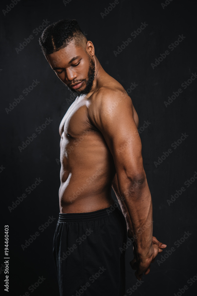 side view of shirtless muscular young african american man stretching hands isolated on black
