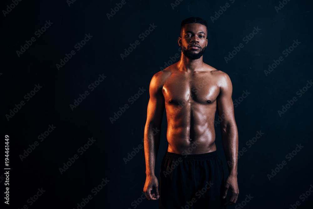 handsome shirtless muscular african american man standing and looking at camera isolated on black