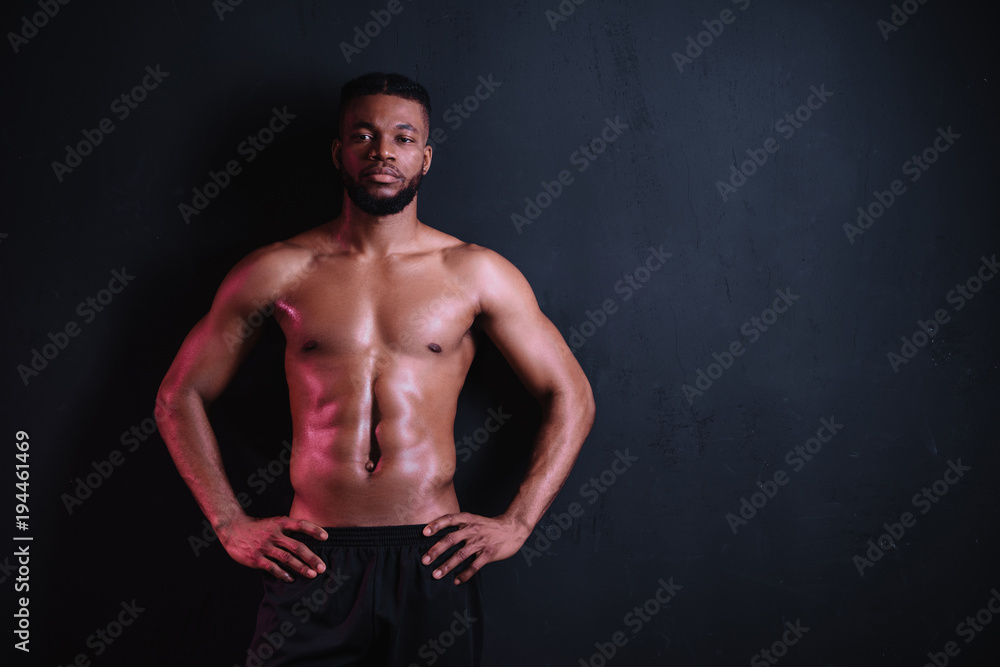 Fototapeta premium muscular bare-chested african american man standing with hands on waist and looking at camera isolated on black