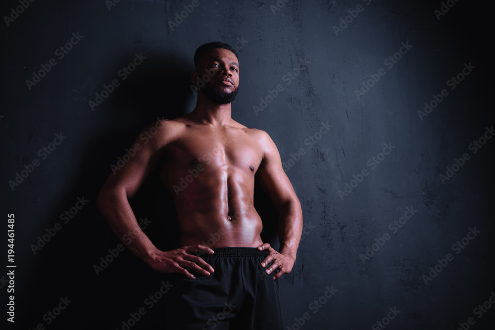 Naklejka premium niski kąt widzenia muskularny, przystojny, młody mężczyzna, stojąc z rękami w pasie i odwracając wzrok na czarno