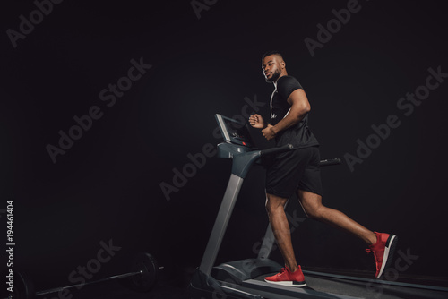 full length view of young african american sportsman running on treadmill on black