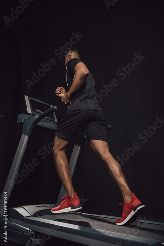 low angle view of young african american sportsman running on treadmill isolated on black