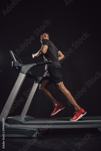 low angle view of young african american sportsman running on treadmill on black