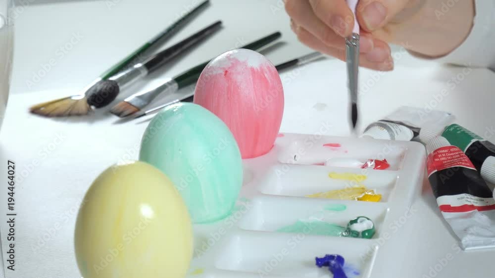 A woman paints Easter eggs with colored paints, close-up A woman paints Easter eggs with colored paints, close-up
