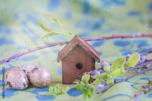 Easter composition with little birdhouse, quail eggs and willow twigs on green background