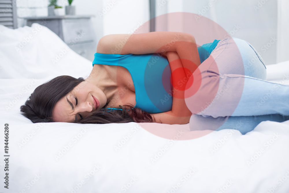 Fototapeta premium Women's pain or menstrual syndrome. A young woman lying on a bed at home holds onto her stomach and curls through spasms.