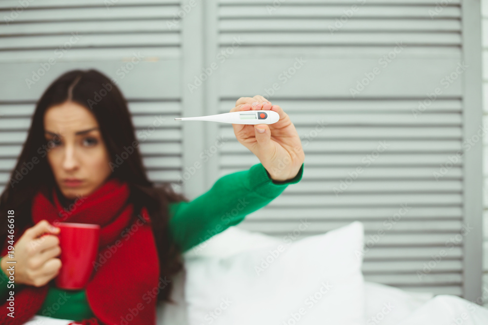 Very high body temperature. A young sick woman in a red scarf measures the temperature with a thermometer. The concept of health and disease. Very high body temperature. A young sick woman in a red scarf measures the temperature with a thermometer. The concept of health and disease.