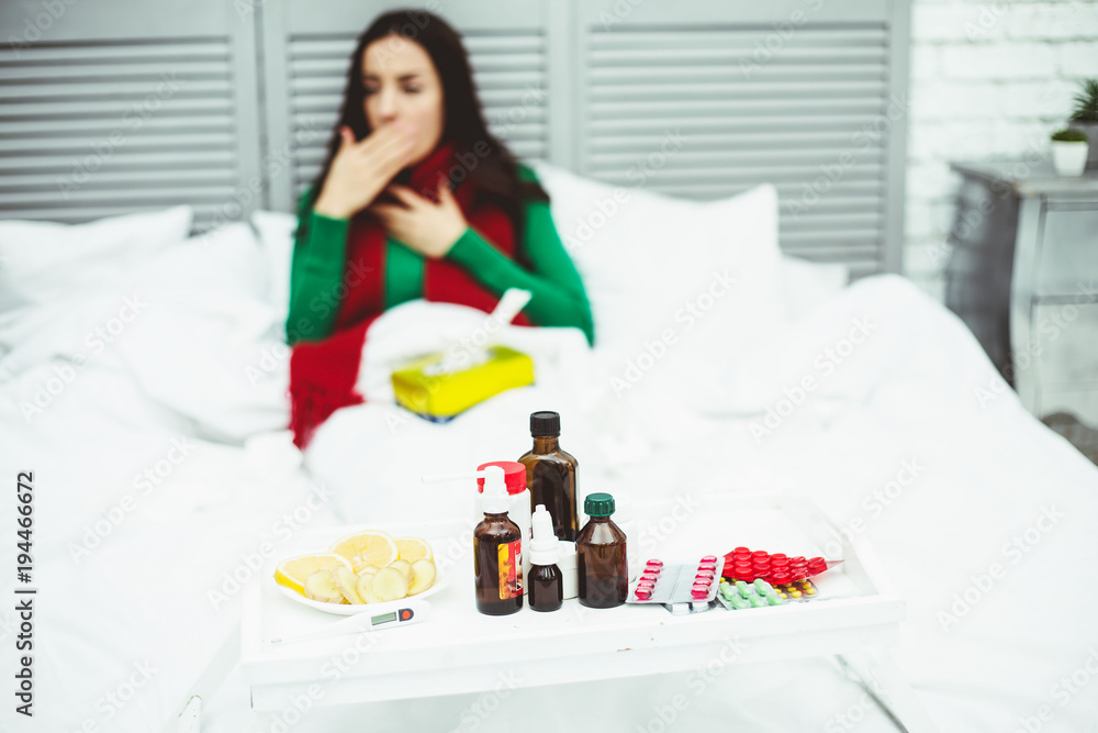 Table with medicines, pills and sprays against the background of a young sick girl in bed. The concept of health and disease.