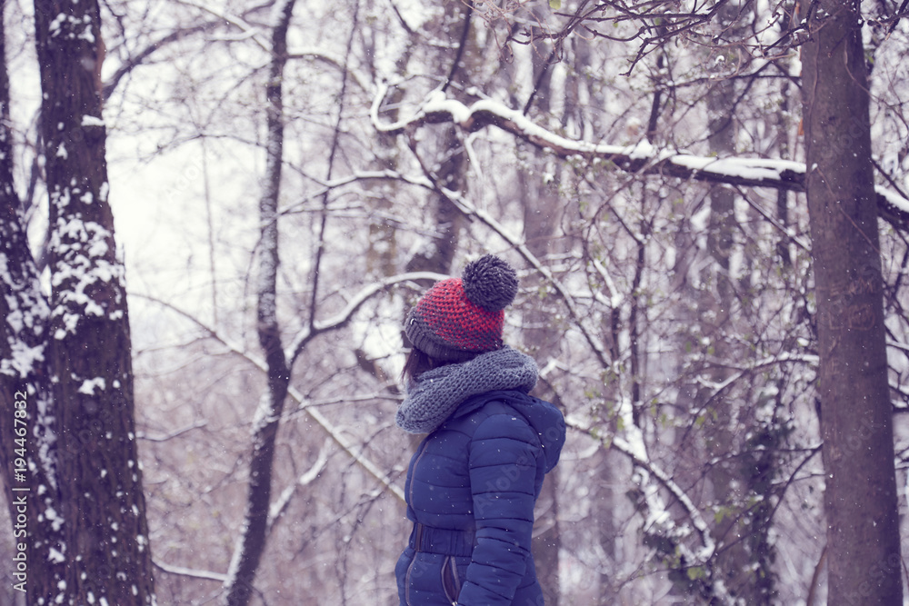 woman head with wool bobble hat in a forest while snowing