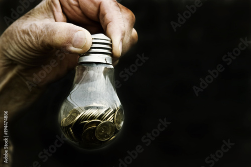 Coins in a glass lamp in old wrinkled hands on a black background close-up