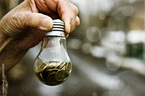 Coins in a glass lamp in old wrinkled hands on a light background