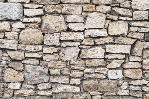 Close-up textured background is an irregular natural stone wall made of different stones without a cement-type bonding mixture. Medieval background