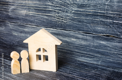 Two people are standing near the house. Wooden figures of persons stand near a wooden house. The concept of a couple in love, cohabitants, parents, buyers and sellers at home.. Sweet Home. photo