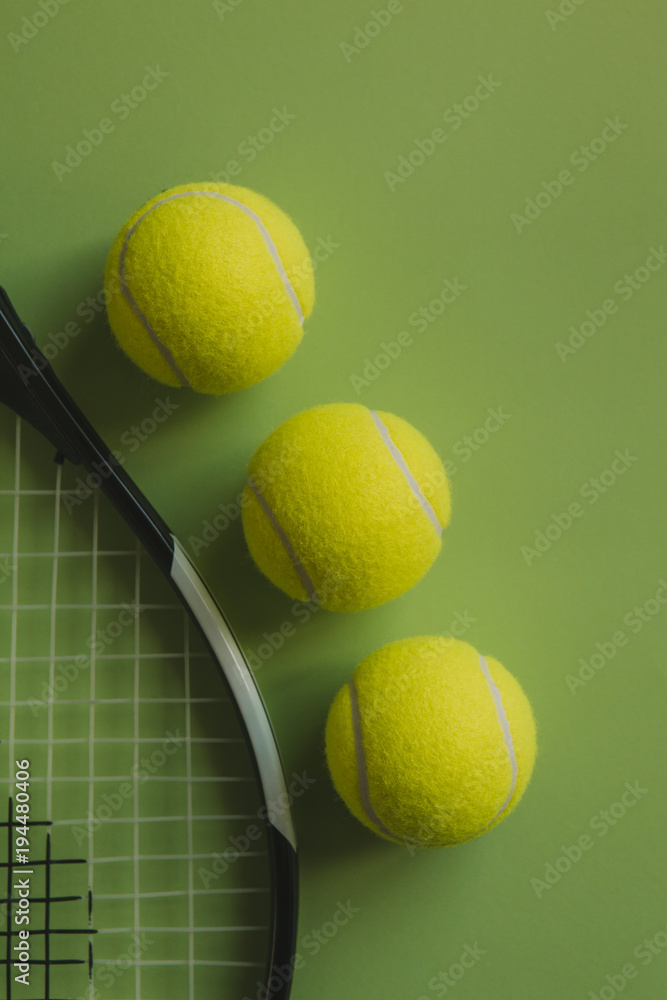 Three tennis balls and a tennis racket on green background.
