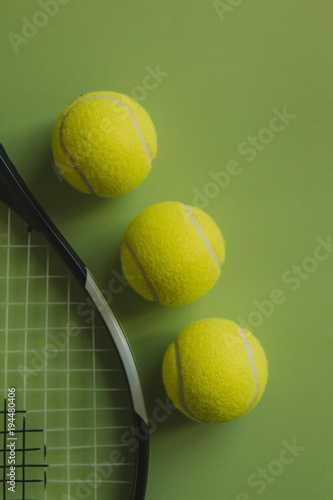 Three tennis balls and a tennis racket on green background.
