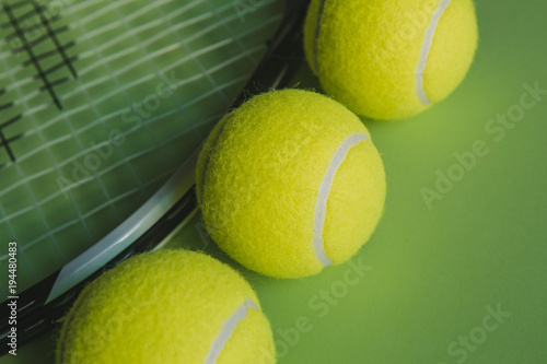 Three tennis balls and a tennis racket on green background. Close up.