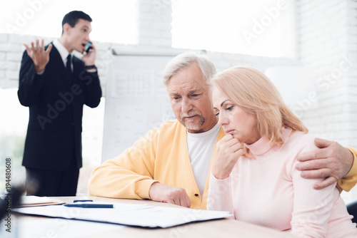 An agitated couple of old people at a reception with a realtor. The realtor is excitedly discussing something on phone.