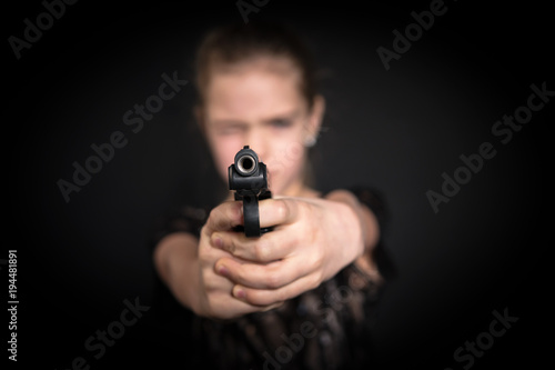 Girl aiming a gun at the camera, blurred background, on black