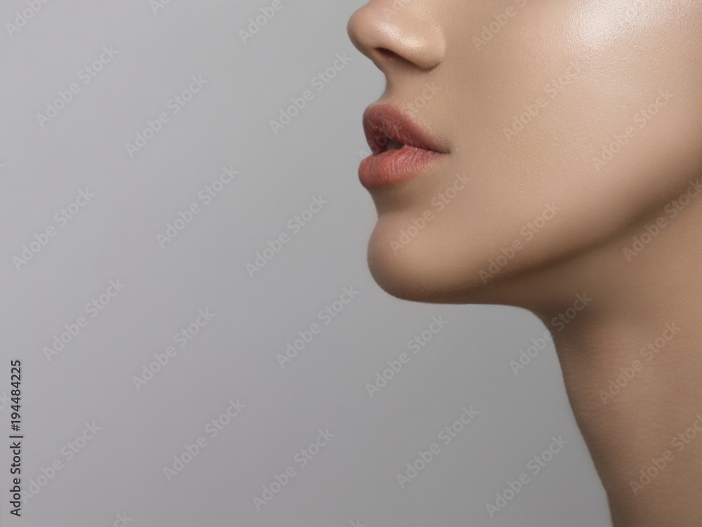 Obraz premium Close-up portret pięknej kobiety czystości twarzy z makijażem nagie usta. Uroczy model z czystą błyszczącą skórą i długą szyją. Miejsce na Twój tekst, szare tło. Daje pocałunek