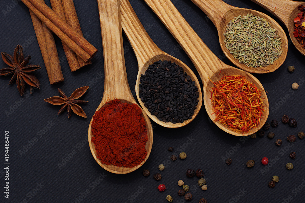 Fototapeta premium Spice. Spice in a wooden spoon. Herbs. Curry, saffron, turmeric, pepper and others on a black background.