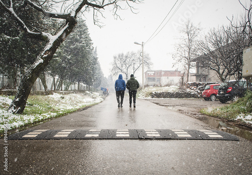 Two guys walking down the street while snowing