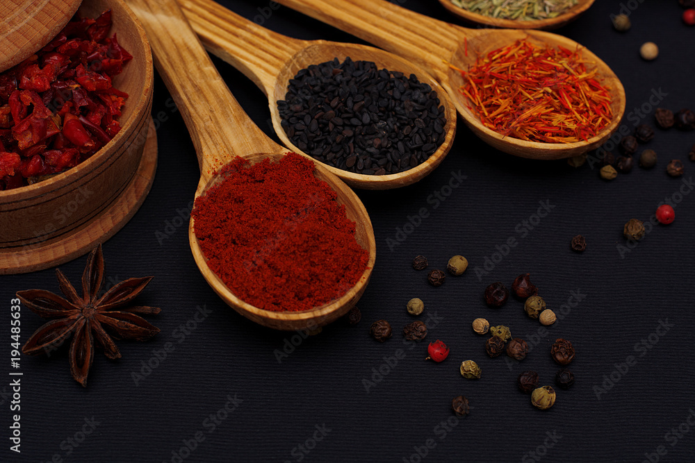 Fototapeta premium Spice. Spice in a wooden spoon. Herbs. Curry, saffron, turmeric, pepper and others on a black background.