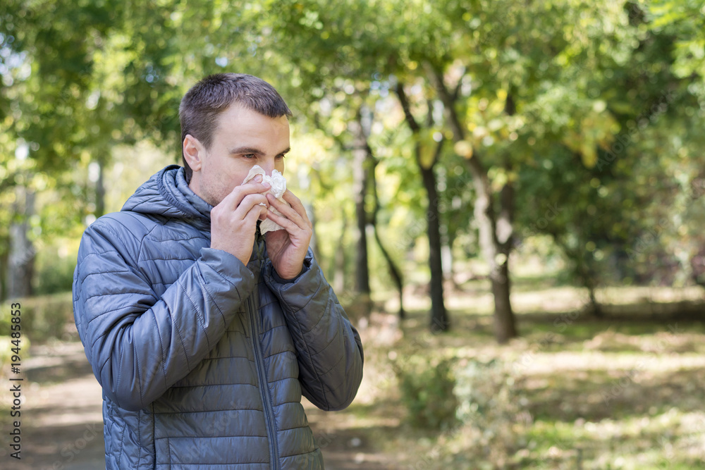 Young man outside blowing nose to paper napkin, sick man Young man outside blowing nose to paper napkin, sick man