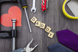 DADDY message on a wooden background with frame of tools and ties.