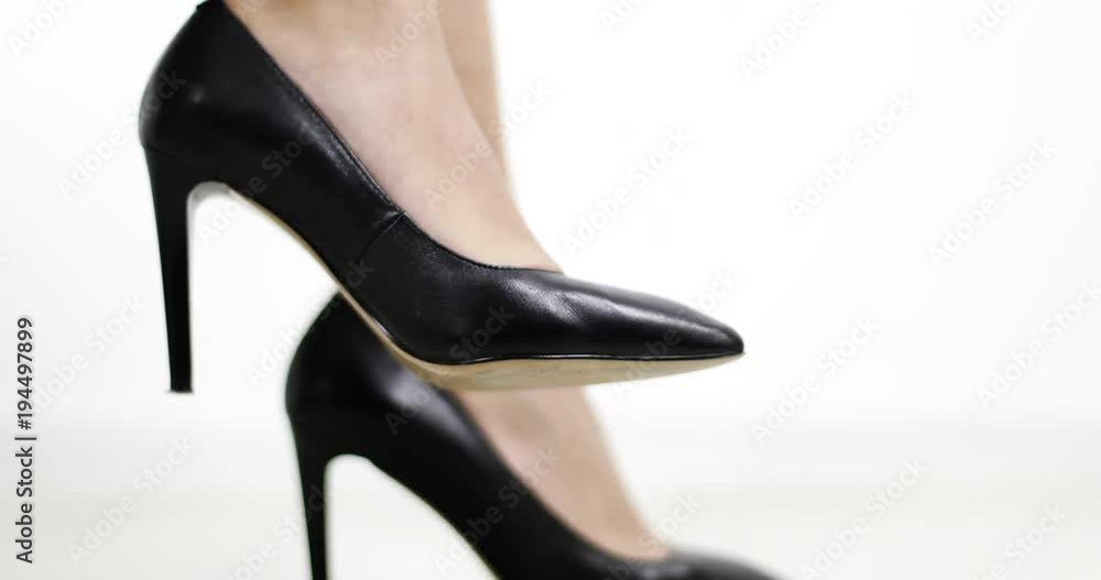 Tanned female legs in black shoes with high heel on a white background.
