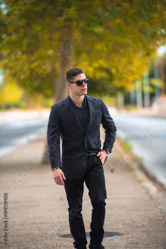 Good looking man in fashion shoot, wear black dress shirt and sunglasses walking on the street © Domforstock