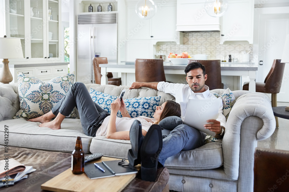 Young Couple relaxing on sofa looking at mobile phone after work Young Couple relaxing on sofa looking at mobile phone after work