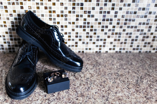 Closeup of elegant stylish black male accessories, isolated on a marble background. gold rings, shoes, cufflinks. Preparation for the concept of a wedding. Horizontal photo copy space