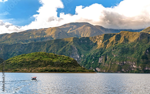 View of the Cuicocha lake and crater, with a small touristic boat in the water, on a sunny and cloudy afternoon. photo