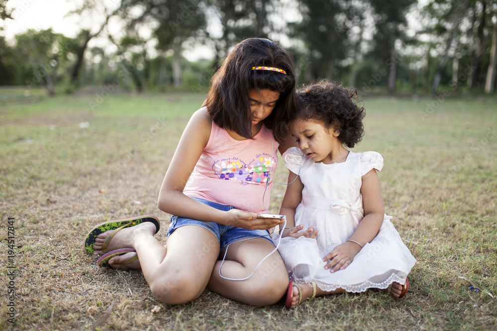 Two Sisters sitting on grass field and browsing smartphone Two Sisters sitting on grass field and browsing smartphone