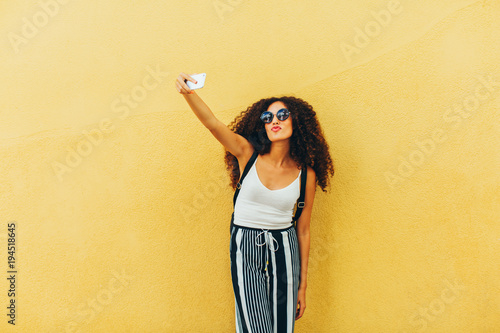 Portrait of a chic tourist taking a selfie in front of a yellow wall. photo