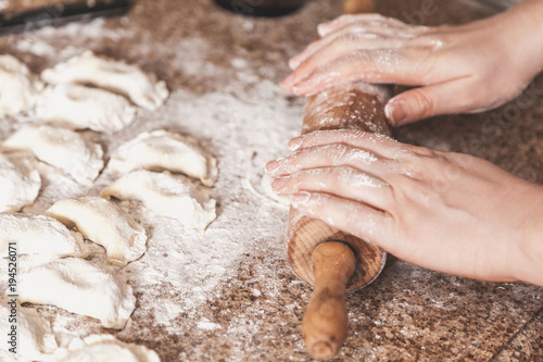 Female hands roll out dough with wooden rolling pin