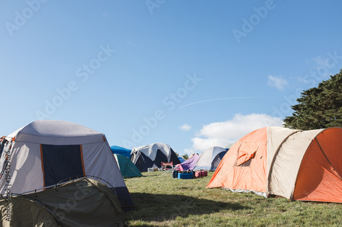 multiple tents set up camping on grass with a blue sky