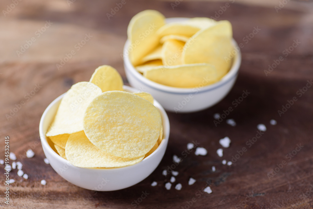Potato chips in a bowl and salt on wooden background Potato chips in a bowl and salt on wooden background