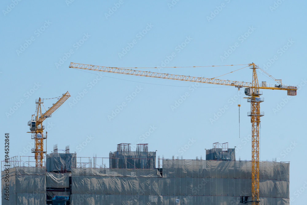 Two yellow construction crane on top of the building under construction site in day time with blue sky background