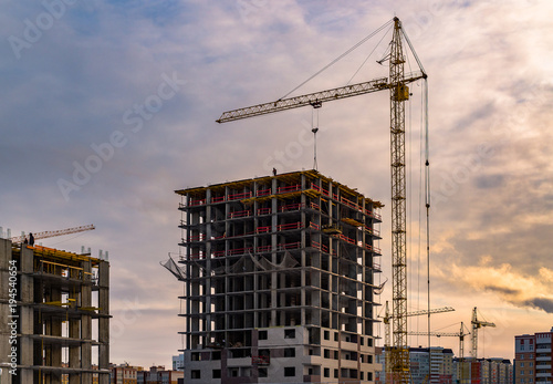 Building crane and building under construction. Construction site. Construction cranes and high rise building under construction against cloudy sky