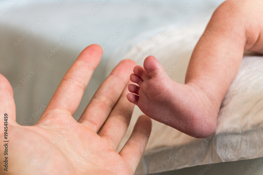 The hand of an adult touches the small foot of the infant The hand of an adult touches the small foot of the infant