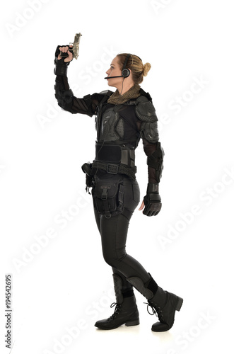 full length portrait of female soldier wearing black tactical armour, holding a gun, isolated on white studio background.